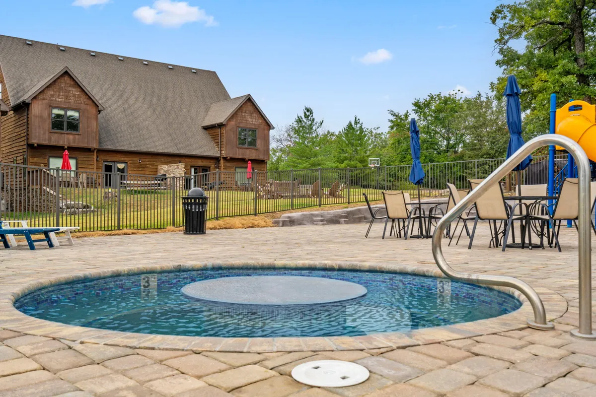 A comprehensive view of the resort's outdoor amenities including a swimming pool, hot tub, seating area, playground equipment, and the house facade. Children are seen playing, families are relaxing in the hot tub, and groups are socializing, all in a family-friendly, leisurely environment.