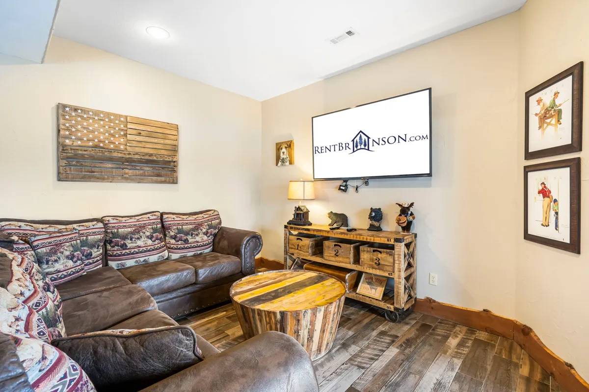 A cozy, inviting lounge area featuring a plush sofa, a wooden coffee table, and a large TV mounted on the wall. The decor is warm and welcoming, ideal for relaxing movie nights or catching up with friends and family.