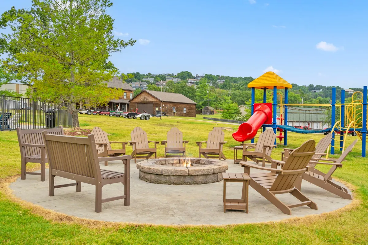An inviting fire pit surrounded by Adirondack chairs, with a nearby playground and a slide. Children can be seen playing, while adults gather around the fire pit, suggesting cozy evenings and multi-generational fun.