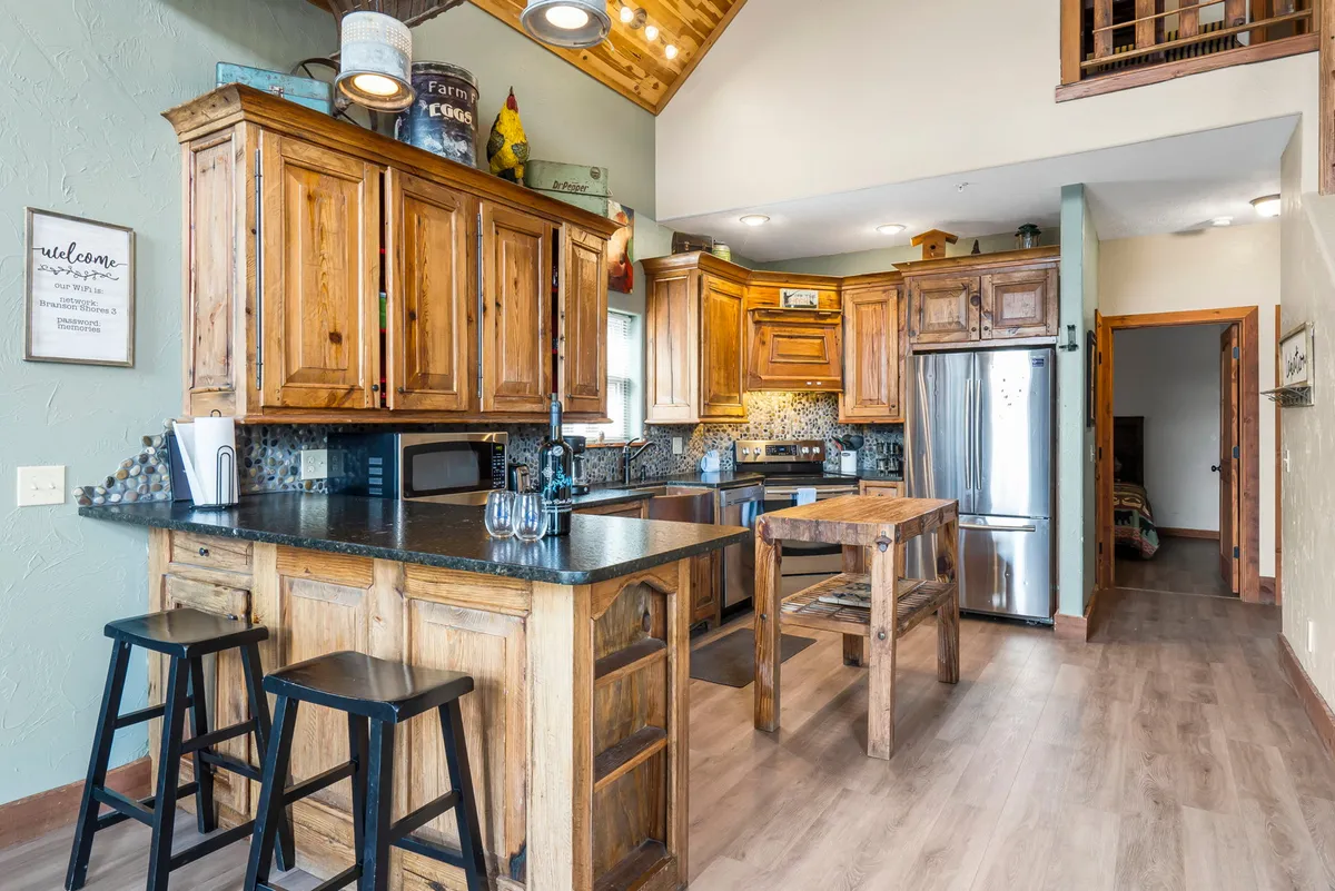 A warm, functional kitchen with wooden cabinets, a central island countertop with stools for casual seating, and updated appliances. The space is designed for both meal preparation and social interaction.