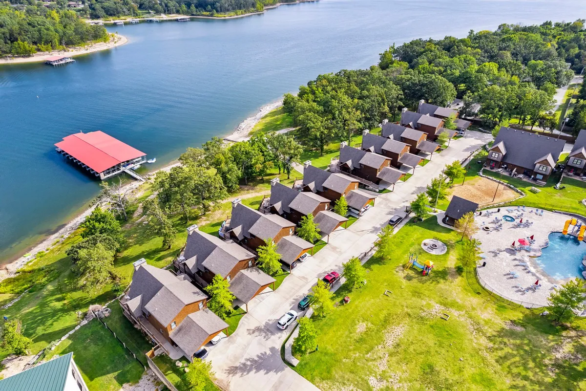 The image displays a sweeping lakefront view with cabins and a pool area, inviting scenes of families swimming, fishing, and gathering outdoors. The communal and recreational atmosphere captures the lakeside retreat experience after a day exploring Branson and Silver Dollar City.