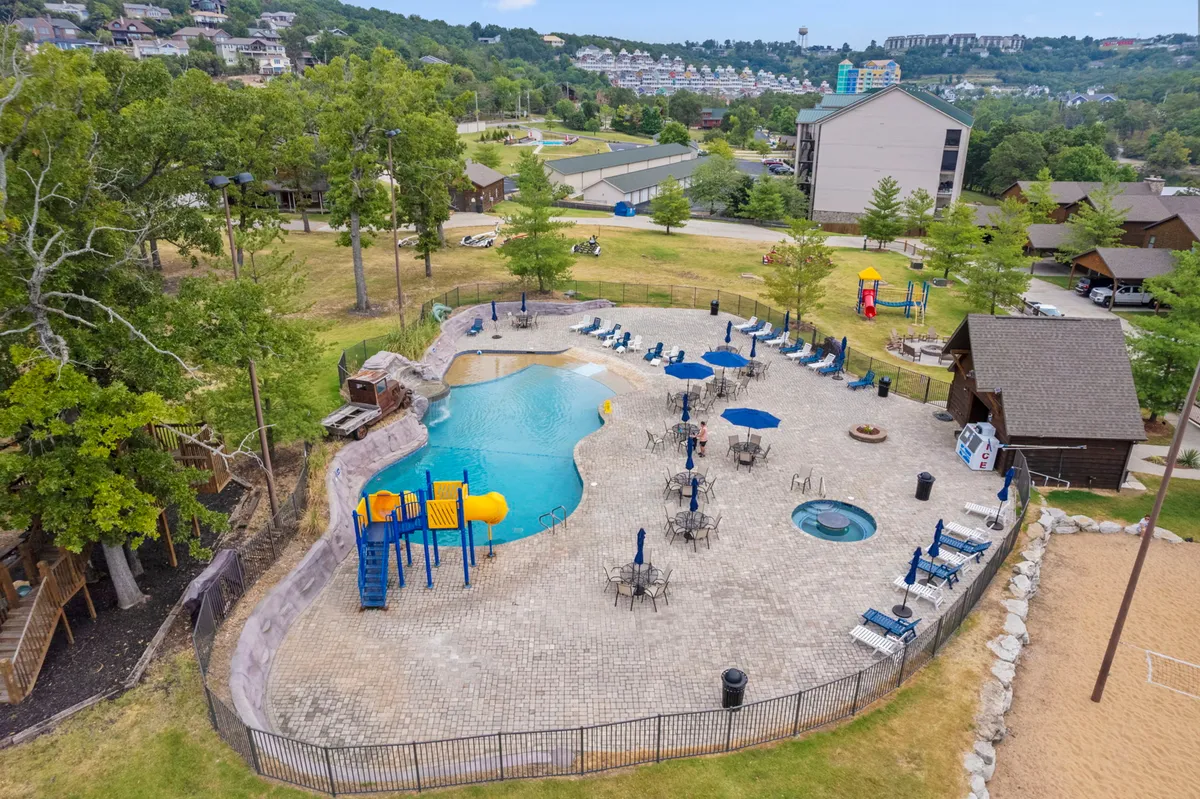 A wide-angle view of the resort’s main amenities, including the swimming pool, hot tub, playground equipment, lounge chairs, and sand volleyball court. The scene teems with cheerful families enjoying each space, emphasizing variety and communal fun.