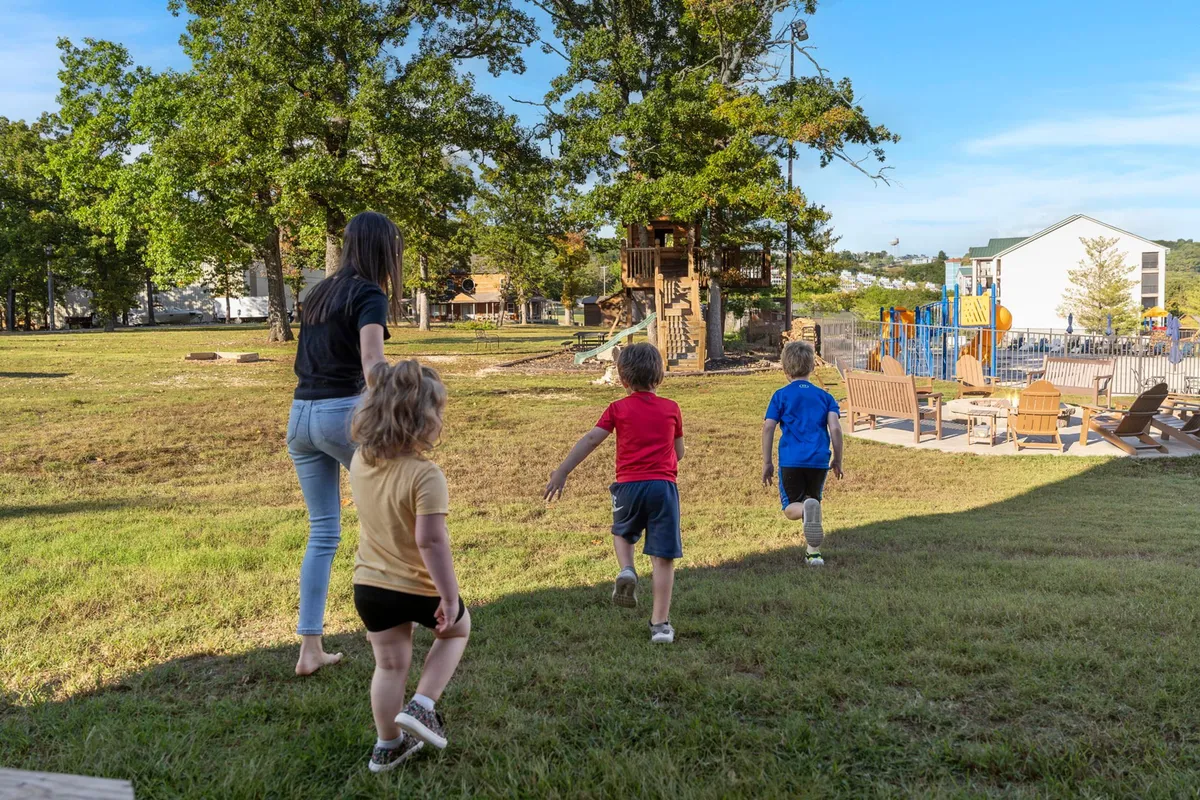 Children are seen running toward a vibrant playground, with adirondack chairs in the foreground and a play structure behind. The scene is full of energy and excitement, showcasing the family-friendly amenities that keep kids entertained close to home.
