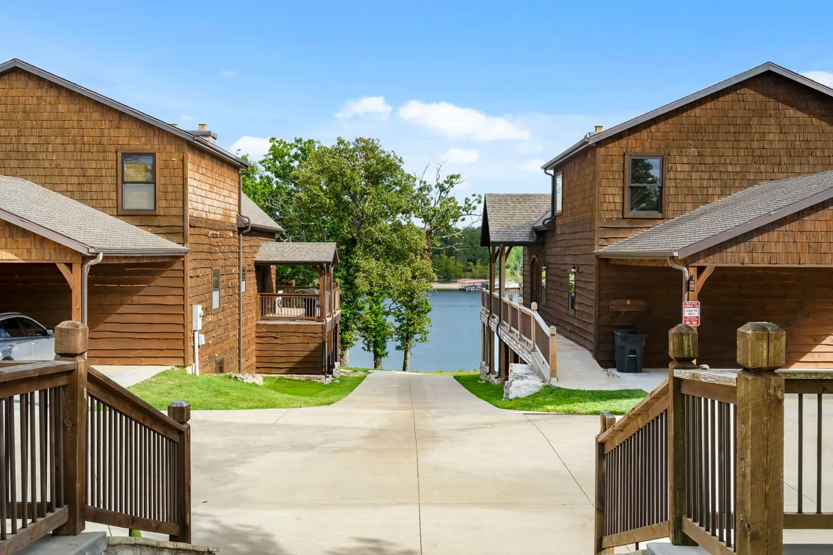 This image showcases wooden cabins set amid green trees with a clear view of the lake and a walkway leading through the landscape. The natural setting suggests opportunities for lakeside walks, exploration, and outdoor family moments.