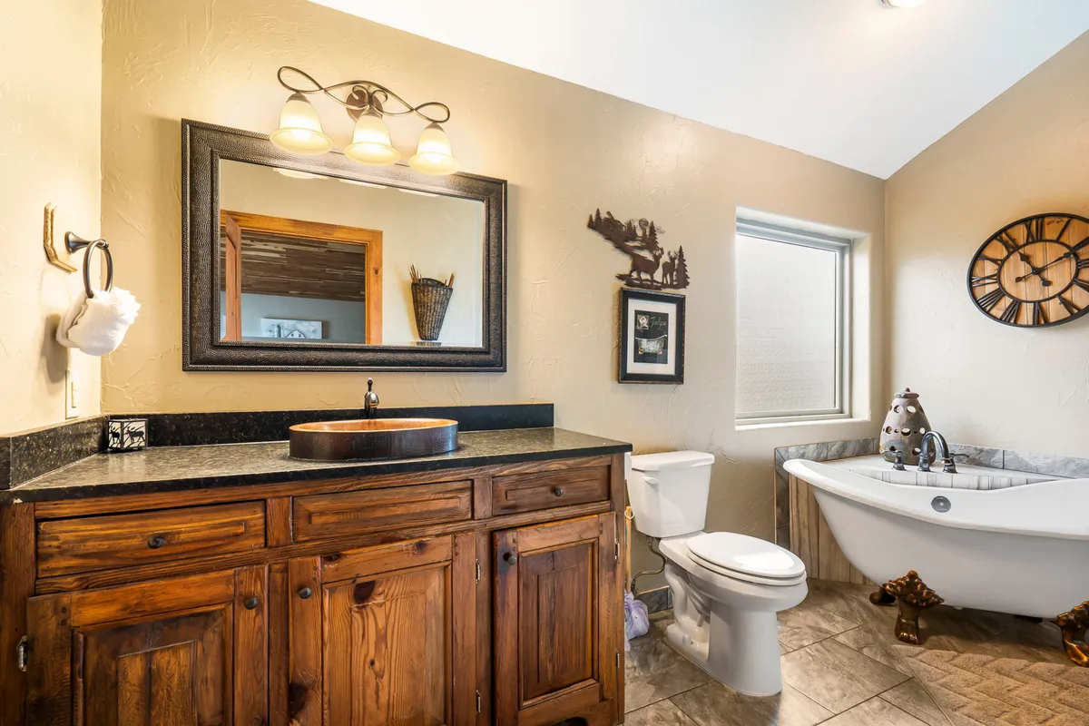 A serene ensuite bathroom featuring a freestanding bathtub, a vanity with sink, large mirror, and tasteful decorative wall art. The atmosphere is tranquil and luxurious, ideal for unwinding after a long day.